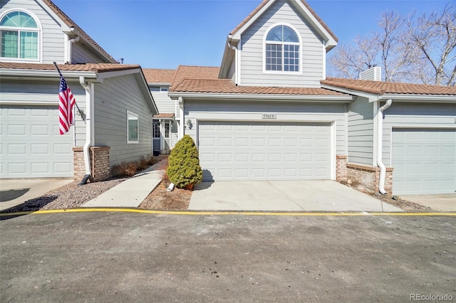 view of front facade with an attached garage, brick siding, a tile roof, driveway, and a chimney