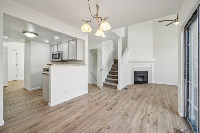 kitchen with a tiled fireplace, stainless steel microwave, light wood-type flooring, and decorative light fixtures