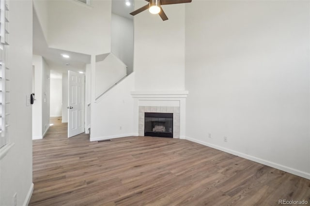 unfurnished living room with a fireplace, a high ceiling, a ceiling fan, wood finished floors, and baseboards