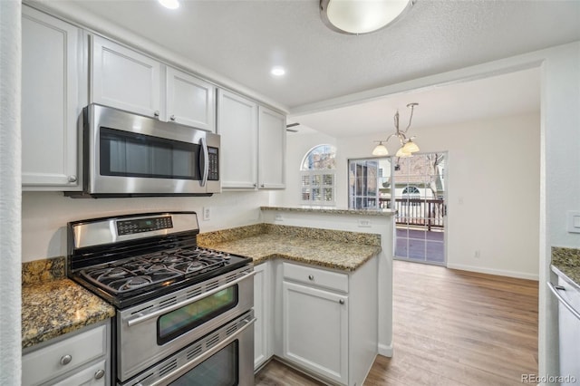 kitchen featuring light wood finished floors, a peninsula, appliances with stainless steel finishes, and stone counters