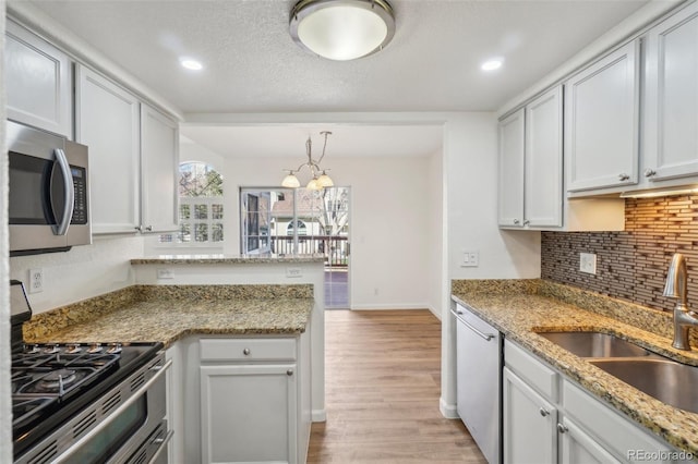 kitchen featuring decorative backsplash, a peninsula, stainless steel appliances, light wood-style floors, and a sink