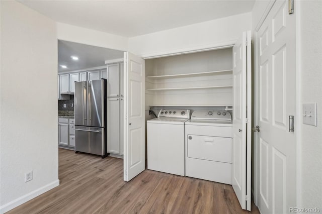 washroom featuring laundry area, wood finished floors, washing machine and clothes dryer, and baseboards