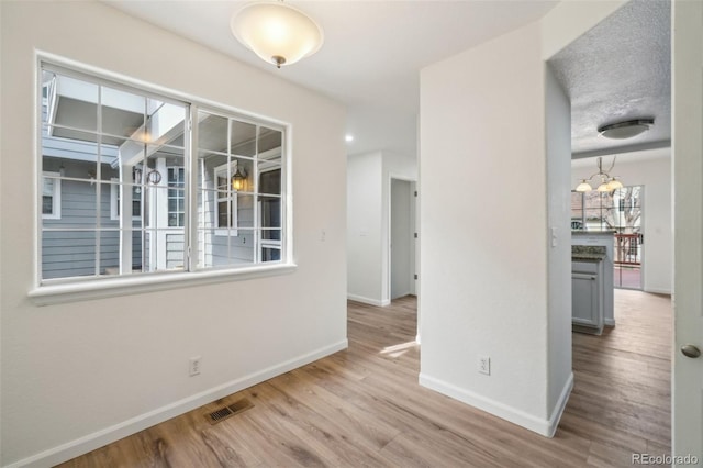 empty room featuring a chandelier, visible vents, baseboards, and wood finished floors