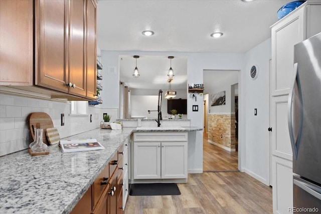 kitchen with freestanding refrigerator, a peninsula, brown cabinets, light wood-style flooring, and hanging light fixtures