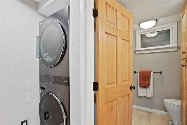 laundry room with laundry area, baseboards, stacked washing maching and dryer, a textured ceiling, and light wood finished floors