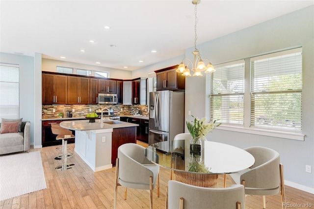 kitchen featuring a sink, light countertops, appliances with stainless steel finishes, an island with sink, and pendant lighting