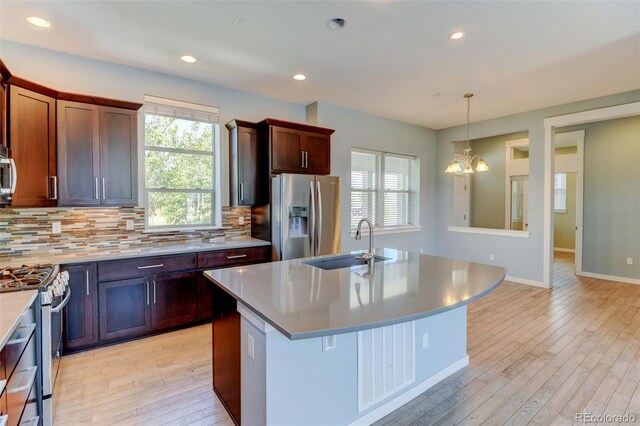 kitchen featuring stainless steel appliances, light countertops, backsplash, a kitchen island with sink, and a sink