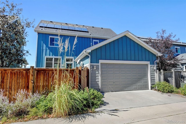 view of front facade featuring a garage, solar panels, concrete driveway, fence, and board and batten siding