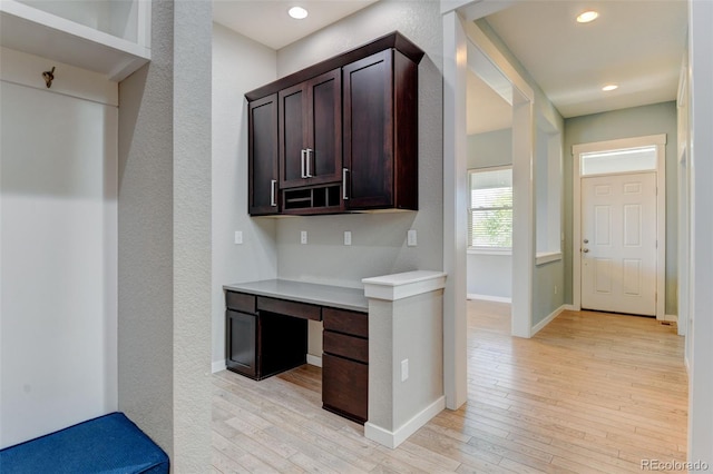 kitchen featuring light wood finished floors, baseboards, light countertops, dark brown cabinets, and built in desk