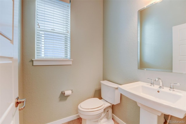 half bath with toilet, baseboards, and a sink