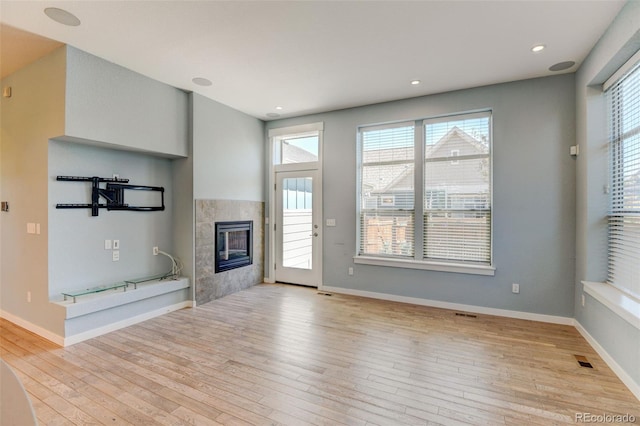 unfurnished living room with light wood finished floors, a fireplace, visible vents, and baseboards