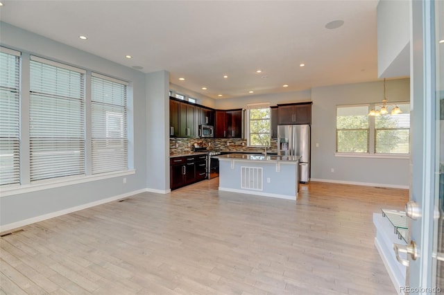 kitchen with light wood finished floors, tasteful backsplash, an inviting chandelier, stainless steel appliances, and light countertops