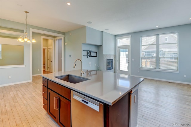 kitchen featuring hanging light fixtures, light wood-style flooring, stainless steel dishwasher, a kitchen island with sink, and a sink