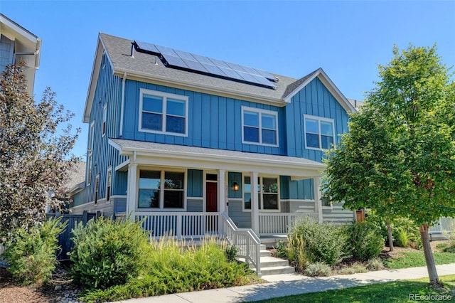 view of front of house with a porch, roof mounted solar panels, and board and batten siding