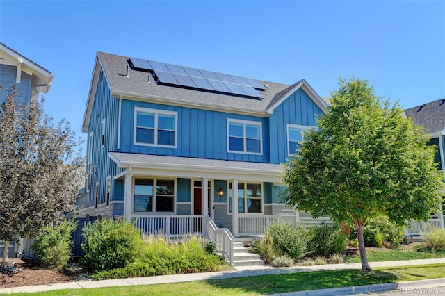 view of front of property with board and batten siding, roof mounted solar panels, roof with shingles, and a porch