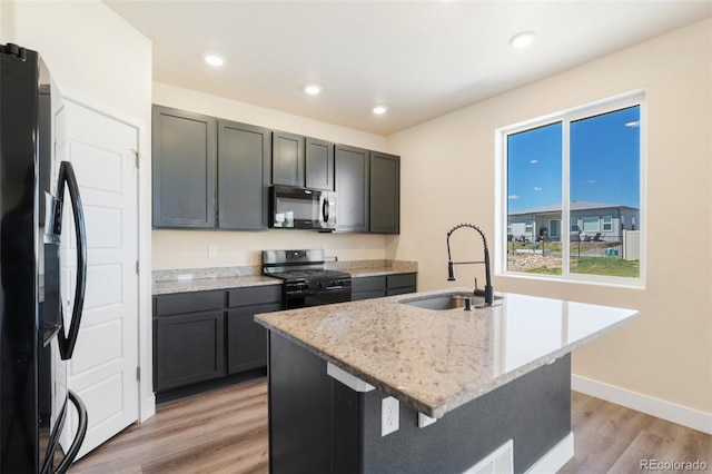9805 Granite Park Ln, Peyton, CO 80831 - kitchen featuring black appliances, light wood-style flooring, light stone countertops, an island with sink, and recessed lighting
