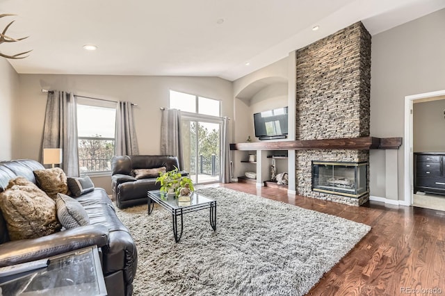 living room featuring wood finished floors, lofted ceiling, a stone fireplace, and recessed lighting