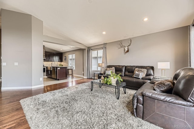 living room featuring wood finished floors, baseboards, vaulted ceiling, and recessed lighting