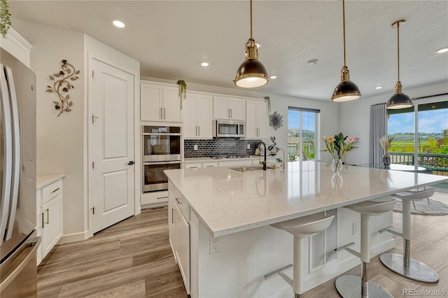 17194 Desert Wine Ln, Parker, CO 80134 - kitchen featuring stainless steel appliances, light wood finished floors, white cabinets, a large island with sink, and tasteful backsplash