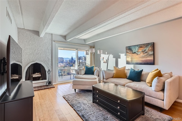 living room featuring hardwood / wood-style floors, beamed ceiling, a large fireplace, and a textured ceiling