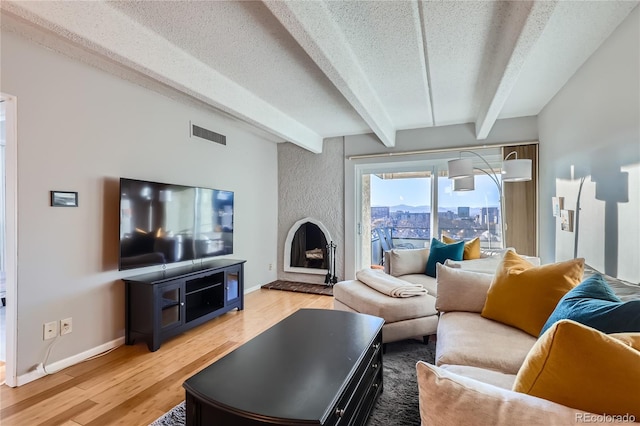 living room featuring beamed ceiling, wood-type flooring, a fireplace, and a textured ceiling