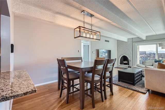 dining area featuring beamed ceiling, a large fireplace, hardwood / wood-style floors, and a textured ceiling