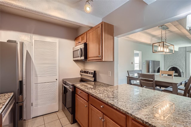 kitchen with pendant lighting, light tile patterned floors, light stone counters, stainless steel appliances, and a textured ceiling