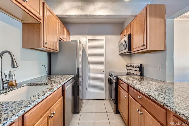 kitchen with stainless steel appliances, sink, light tile patterned floors, and light stone counters