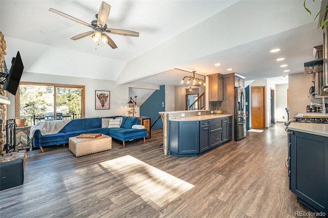 living room featuring ceiling fan with notable chandelier, dark hardwood / wood-style floors, and vaulted ceiling