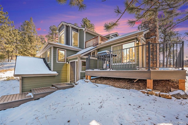 snow covered back of property with a balcony and a wooden deck