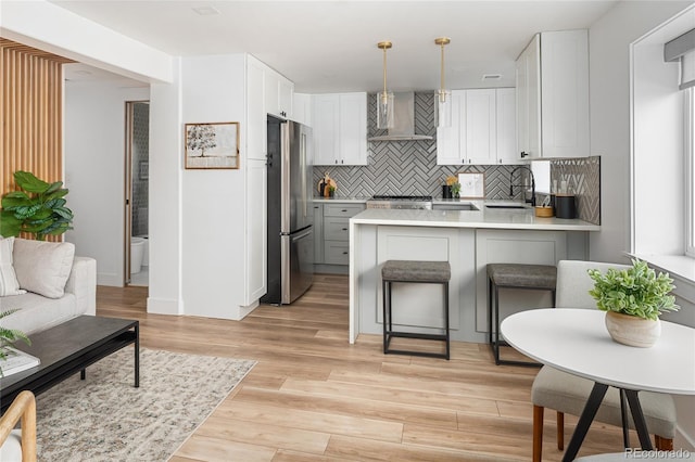 1755 Ingalls St, Lakewood, CO 80214 - kitchen featuring freestanding refrigerator, wall chimney range hood, a peninsula, tasteful backsplash, and light countertops