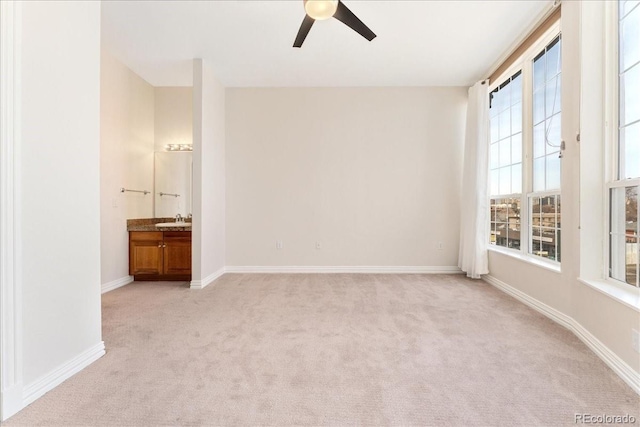 spare room featuring light carpet, a sink, baseboards, and ceiling fan