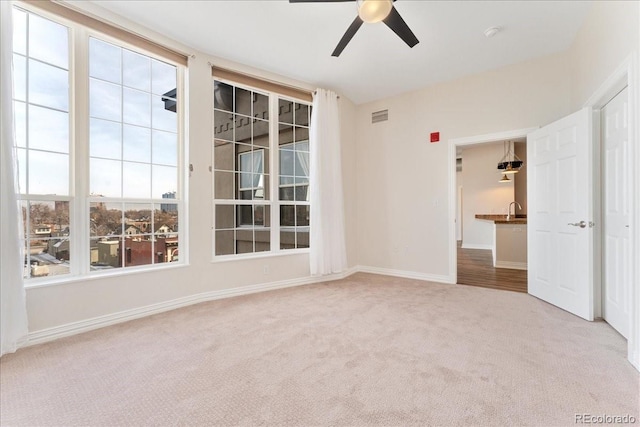 carpeted spare room featuring visible vents, a sink, baseboards, and ceiling fan