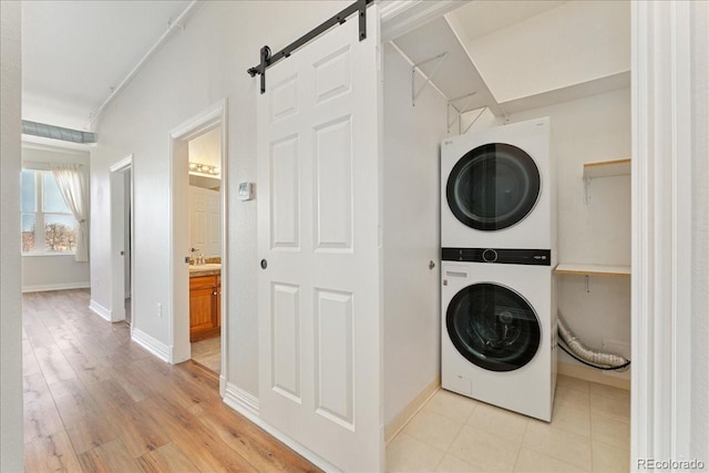 laundry room featuring light wood-style flooring, a barn door, stacked washing maching and dryer, laundry area, and baseboards