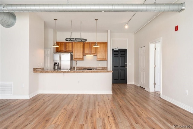 kitchen featuring a peninsula, visible vents, light wood-style floors, stainless steel refrigerator with ice dispenser, and brown cabinetry