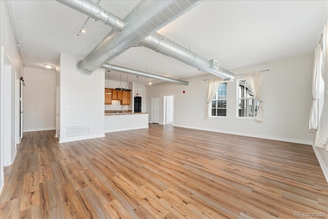 unfurnished living room with track lighting, visible vents, light wood-style flooring, and baseboards