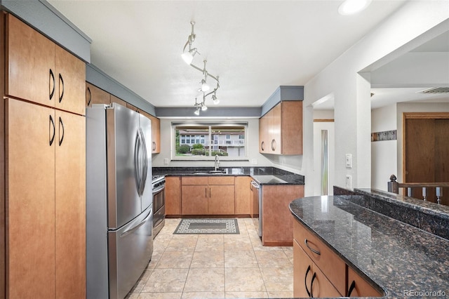 kitchen featuring visible vents, appliances with stainless steel finishes, brown cabinets, a sink, and dark stone countertops
