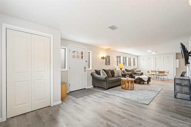 living area with visible vents, baseboards, wood finished floors, and a healthy amount of sunlight