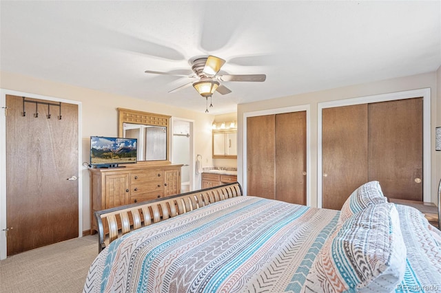 bedroom featuring ceiling fan, ensuite bathroom, two closets, and light carpet