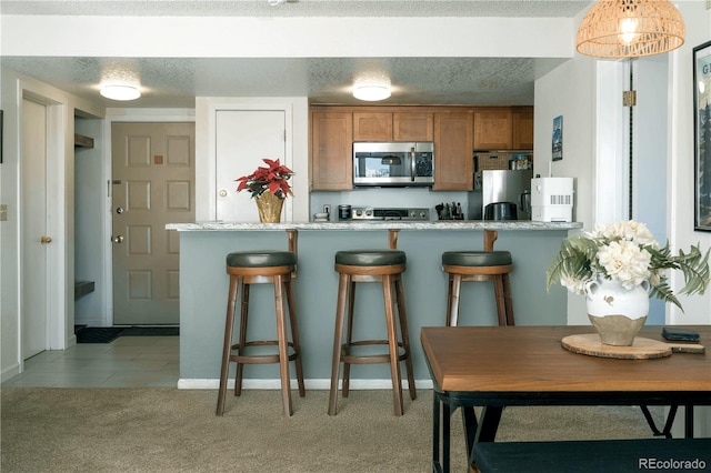 kitchen with appliances with stainless steel finishes, a breakfast bar, light carpet, and light stone counters