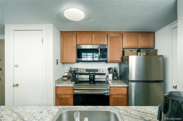 kitchen with stainless steel appliances, light stone countertops, sink, and a textured ceiling