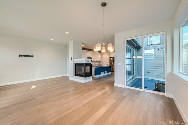 unfurnished living room with a multi sided fireplace, sink, and light hardwood / wood-style floors