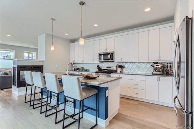 kitchen with white cabinetry, decorative light fixtures, a center island with sink, and appliances with stainless steel finishes