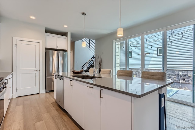 kitchen with sink, white cabinetry, pendant lighting, stainless steel appliances, and a kitchen island with sink