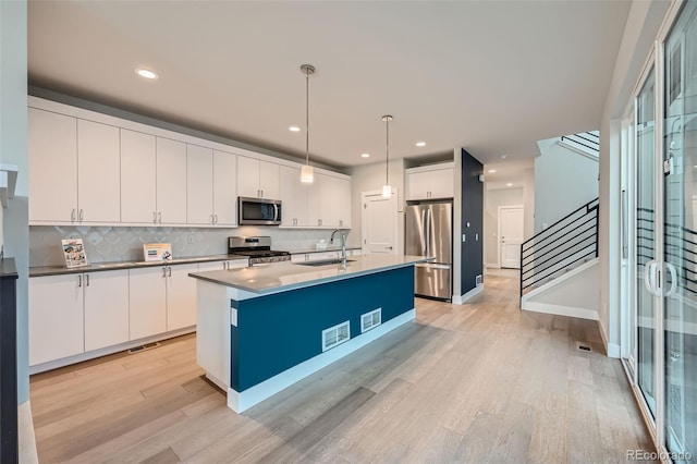 kitchen featuring sink, appliances with stainless steel finishes, a kitchen island with sink, hanging light fixtures, and white cabinets