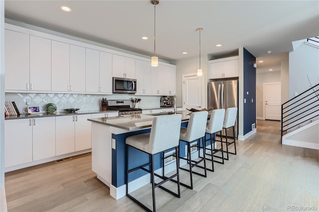 kitchen featuring white cabinetry, a kitchen island with sink, stainless steel appliances, light hardwood / wood-style floors, and decorative light fixtures