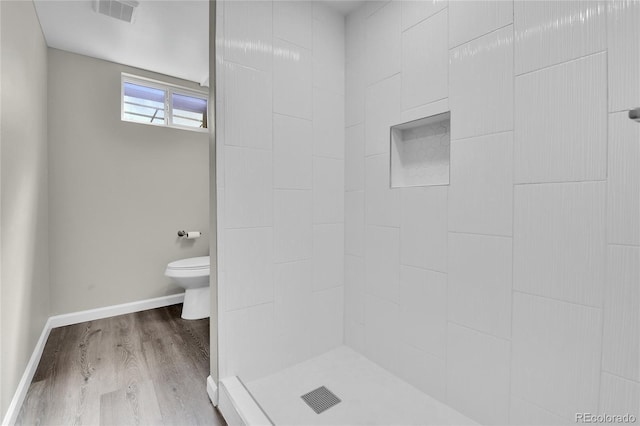 bathroom featuring tiled shower, hardwood / wood-style floors, and toilet