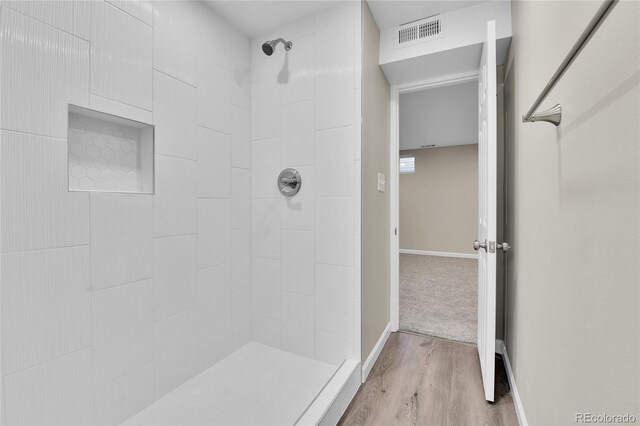 bathroom featuring a tile shower and wood-type flooring