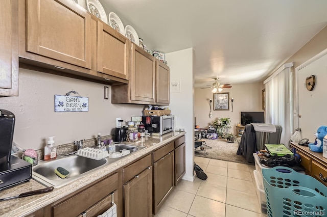 kitchen featuring ceiling fan, light countertops, a sink, stainless steel microwave, and light tile patterned flooring