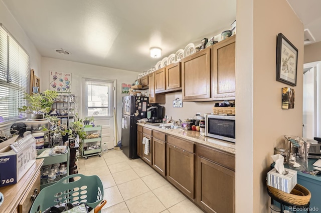 kitchen featuring brown cabinets, light countertops, stainless steel microwave, freestanding refrigerator, and light tile patterned flooring